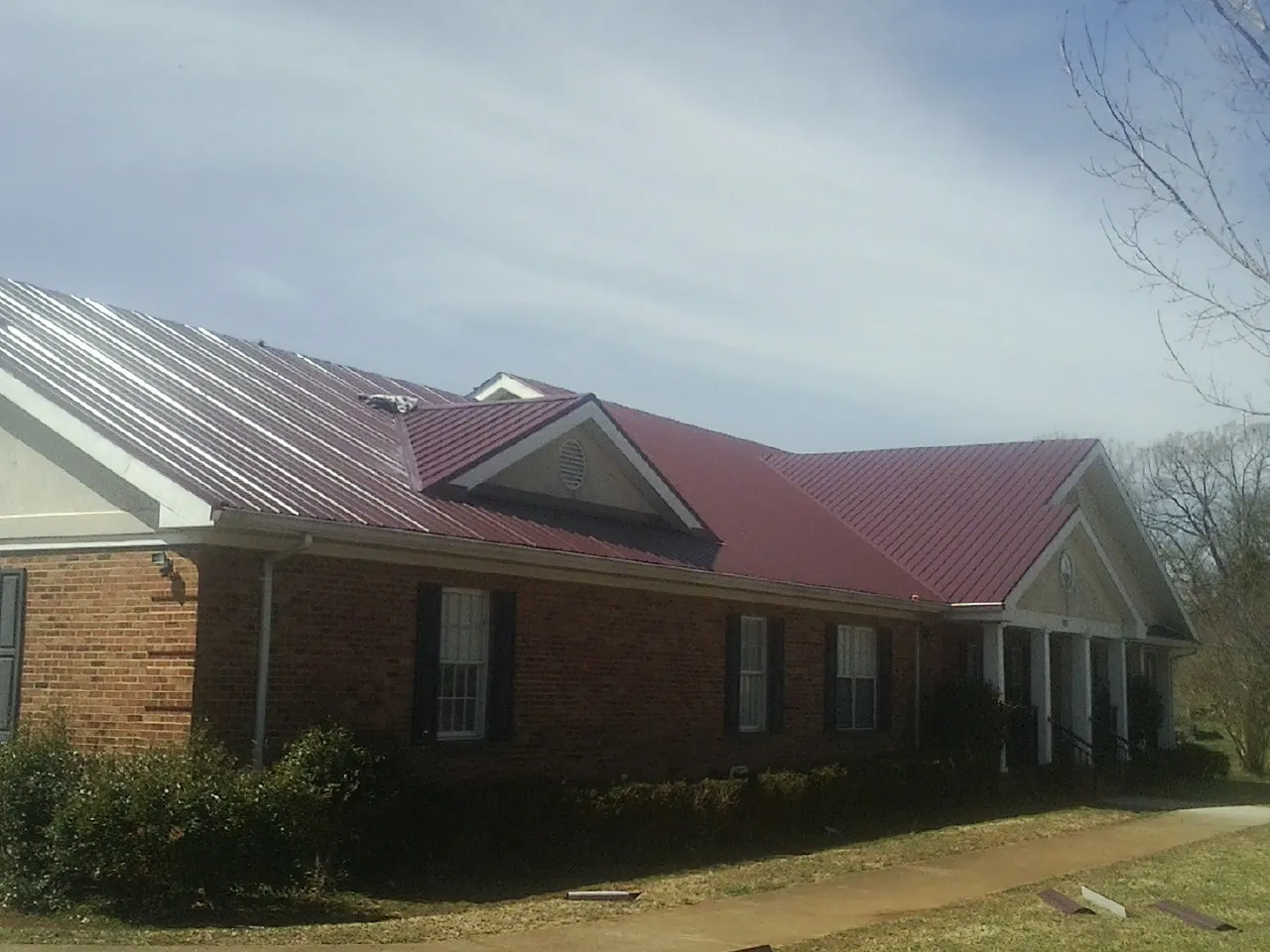 Red metal roof with gabled entries on a long brick building, from a Hail Damage Roof Repair job in Summerville