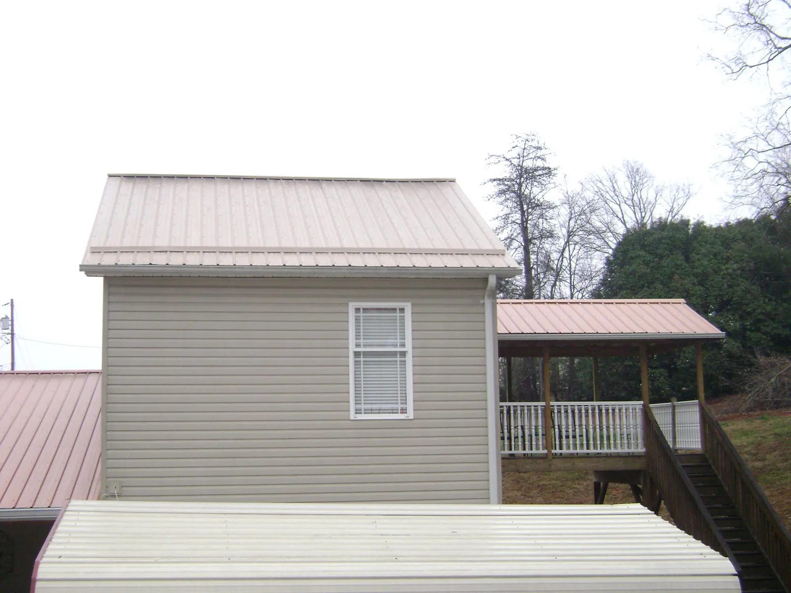 Tan metal roofs on a two story addition and attached porch, from a Roof Replacement job in Summerville